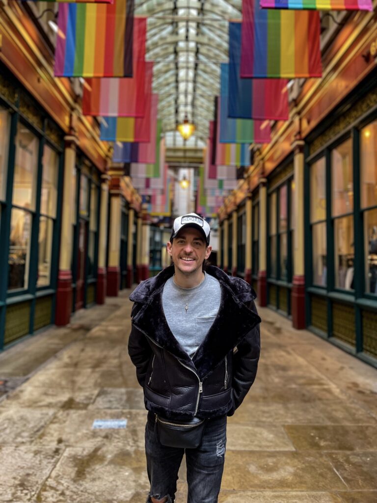 A photo of Ian Helms standing in an alley with Pride flags hanging above